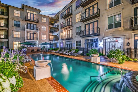 A pool surrounded by a patio and a building with balconies.