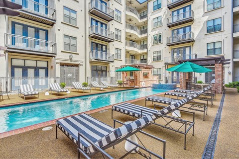 A pool with sun loungers in front of apartment buildings.