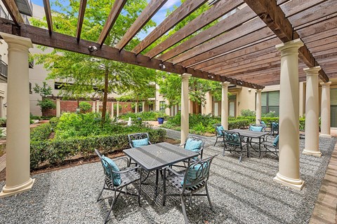 A patio with a table and chairs under a wooden pergola.