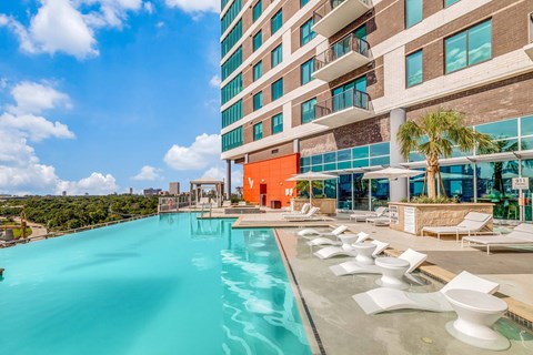 A large swimming pool with white chairs is in front of a modern building.