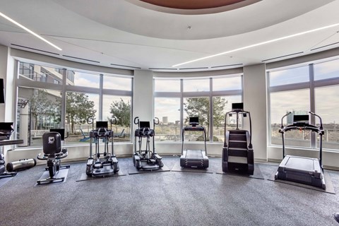 A gym with a row of treadmilers and elliptical machines.