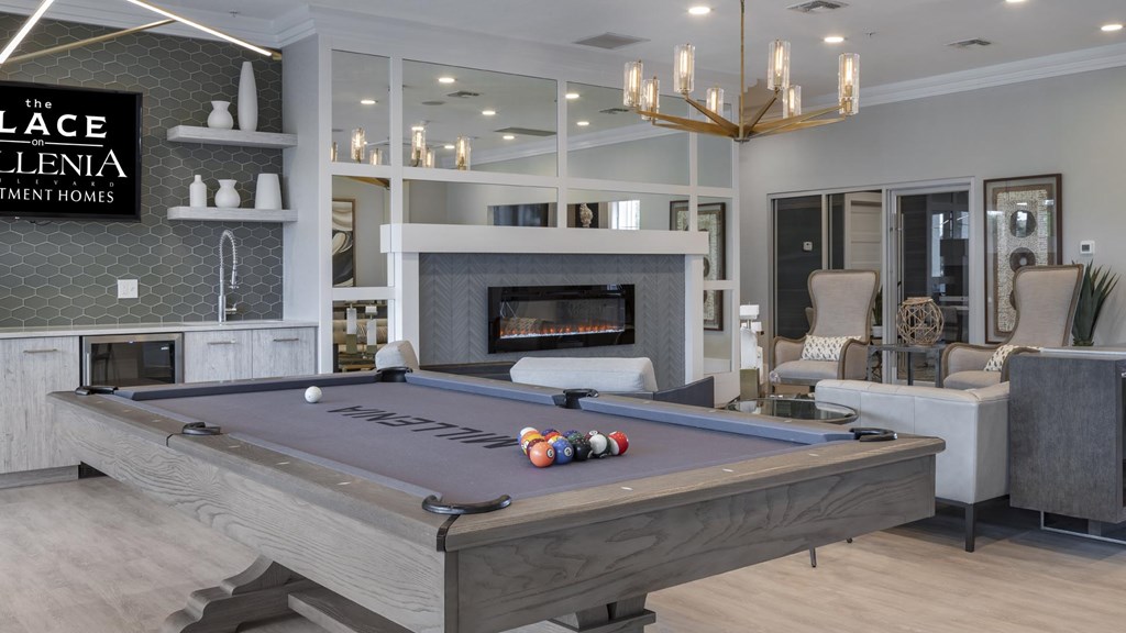 A pool table in a room with a fireplace and a sign that says "The Ellenia Apartment Homes".