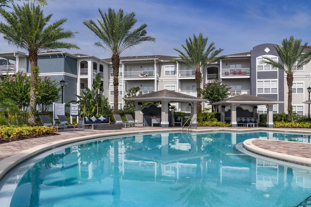A swimming pool in front of a resort with palm trees.
