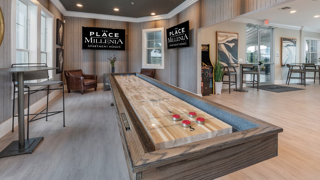 A shuffleboard table is in the middle of a room with wood floors and wood panel walls.