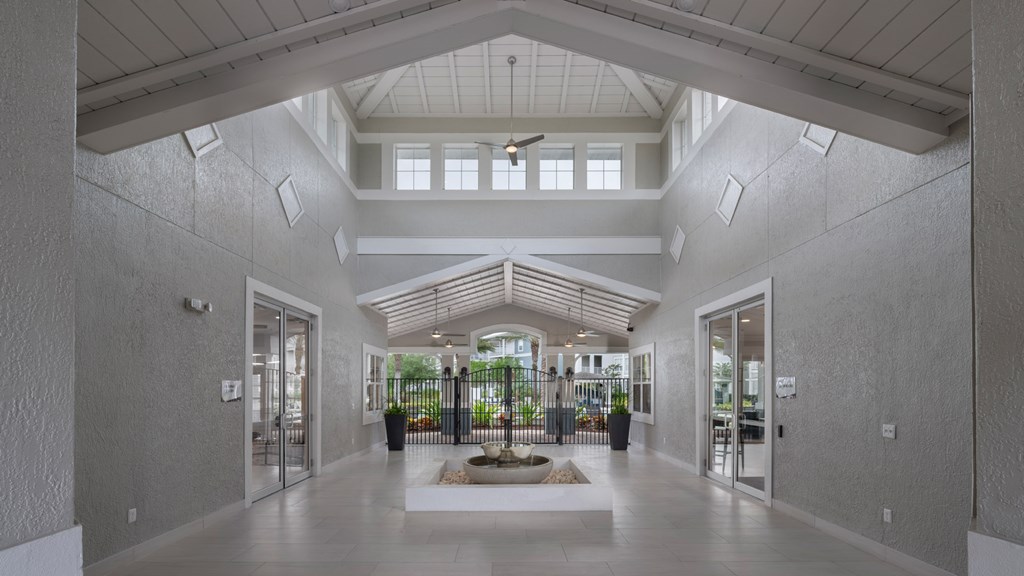 A spacious lobby with a white ceiling and walls, a large rug, and a view of the outdoors through the windows.