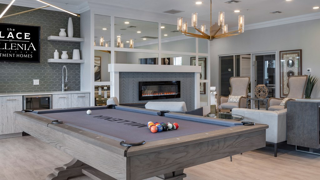 A pool table in a room with a fireplace and a sign that says "The Ellenia Apartment Homes".