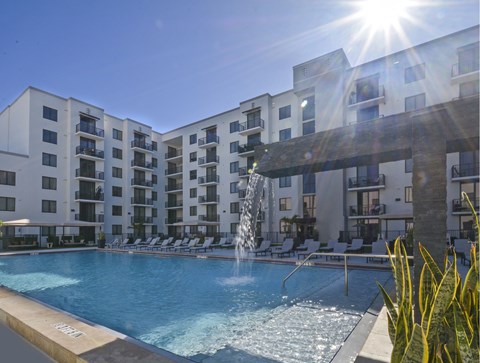 A sunny day at a pool with a fountain in the middle of it.