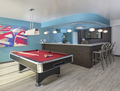 A pool table is in the middle of a room with a bar and stools.