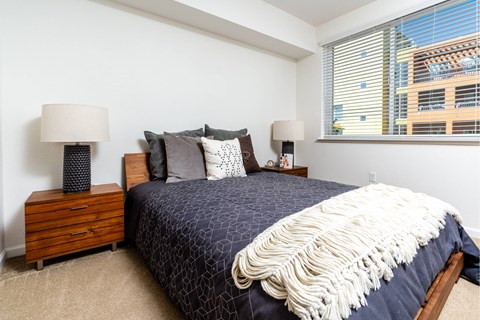 A bedroom with a bed, two lamps, and a window with blinds.