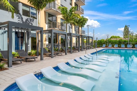 A pool area with sun loungers and a building in the background.
