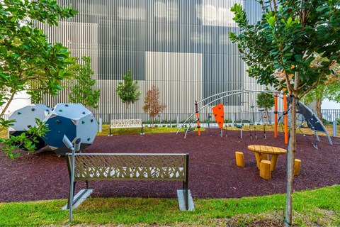 A playground with a blue and white slide, a bench, and a red swing set.