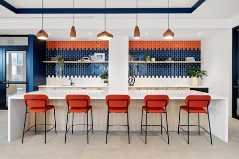 A kitchen with a white counter and orange chairs.