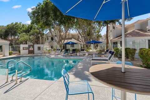 A pool area with a blue umbrella and chairs.