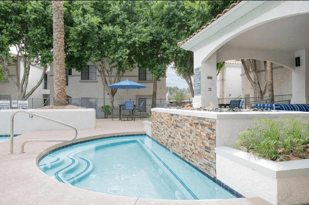 A small pool with a stone wall and a white building in the background.
