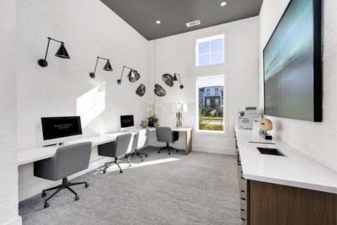 A modern office space with white desks and chairs, a large screen on the wall, and a view of the outside through a window.