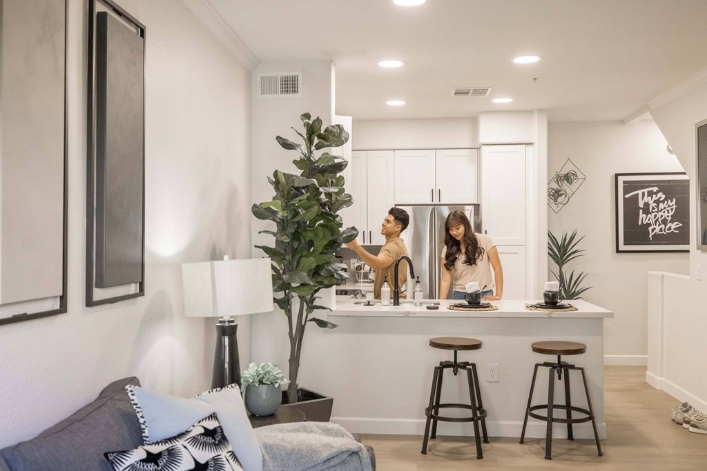 Two people are standing in a kitchen with a bar stool in front of them.