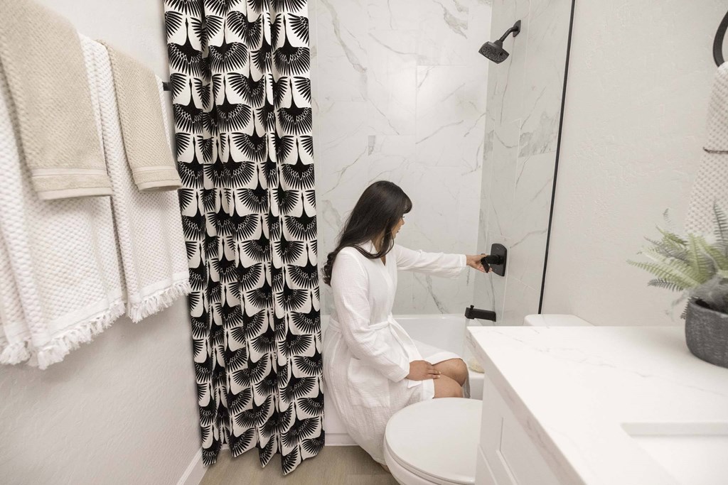 A woman in a white robe is sitting on a toilet in a bathroom.