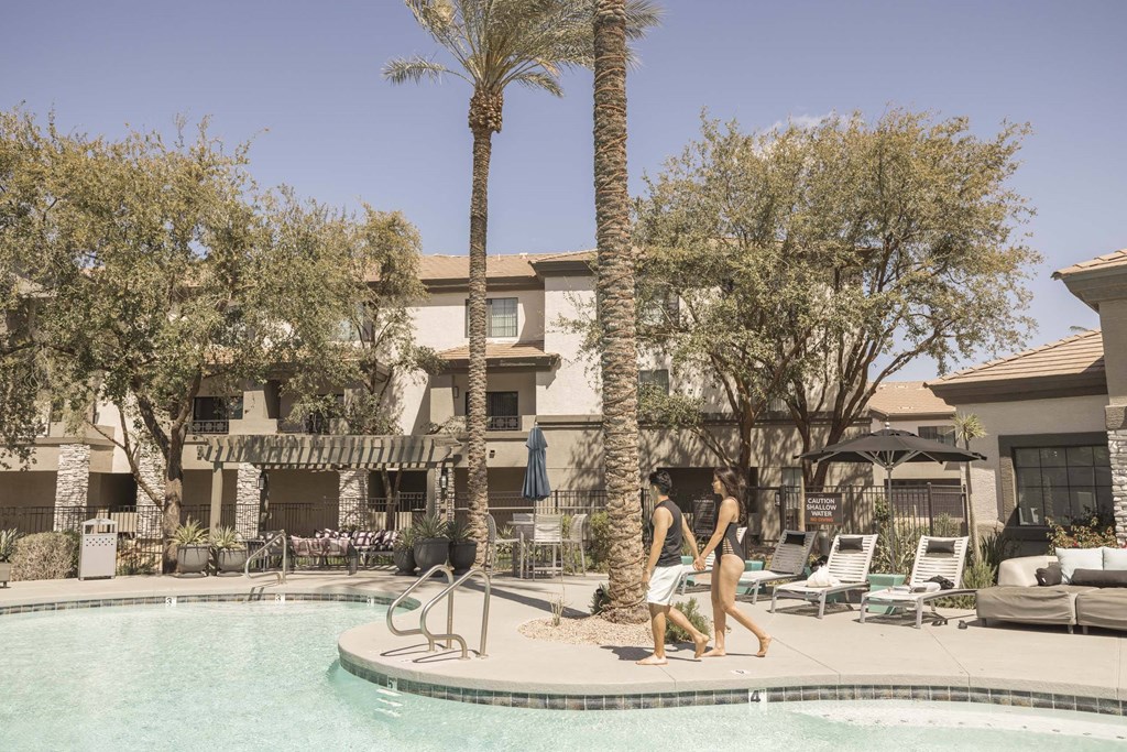 Two people walking by a pool on a sunny day.