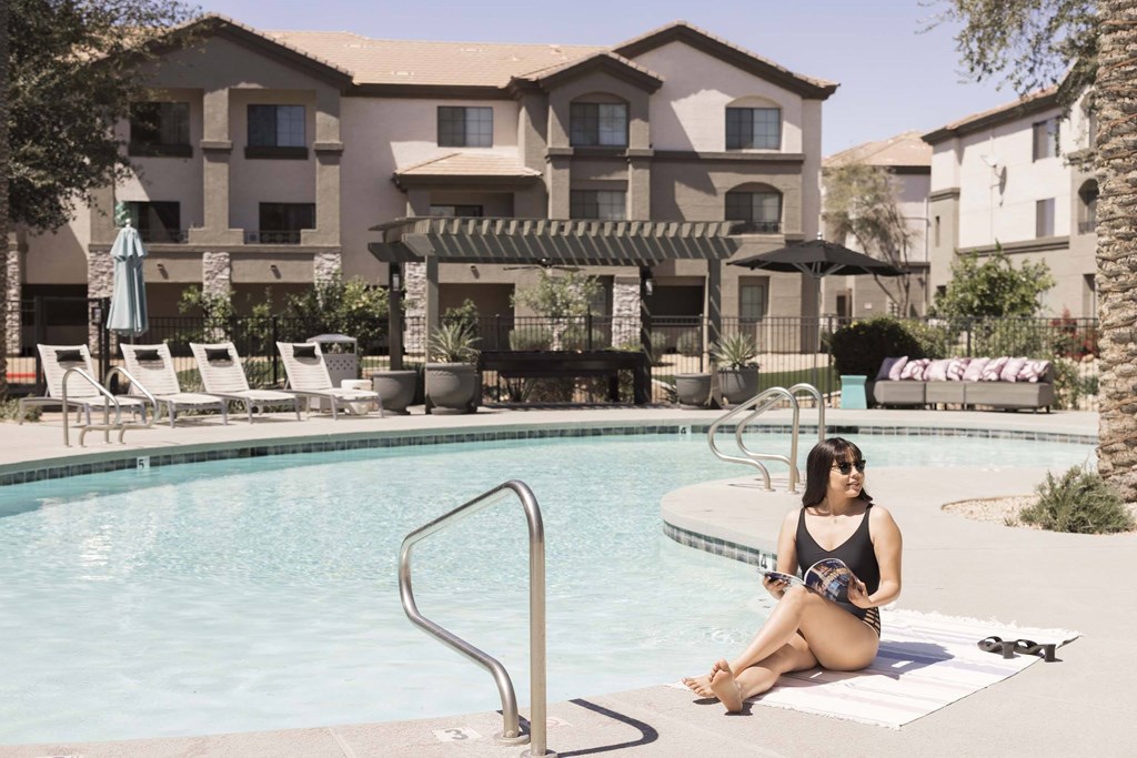 A woman is sitting by a pool in a black swimsuit.