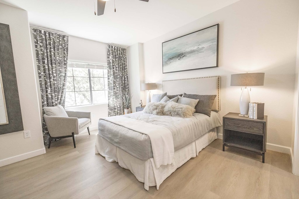 A bedroom with a large bed, a chair, and a painting on the wall.