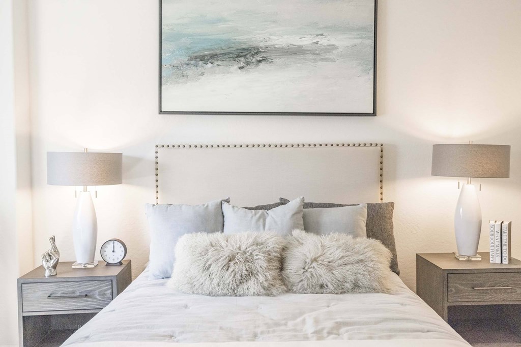 A bedroom with a large bed, two nightstands, and a painting on the wall.