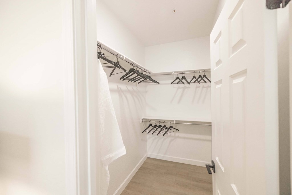 A white closet with clothes hanging on hangers.