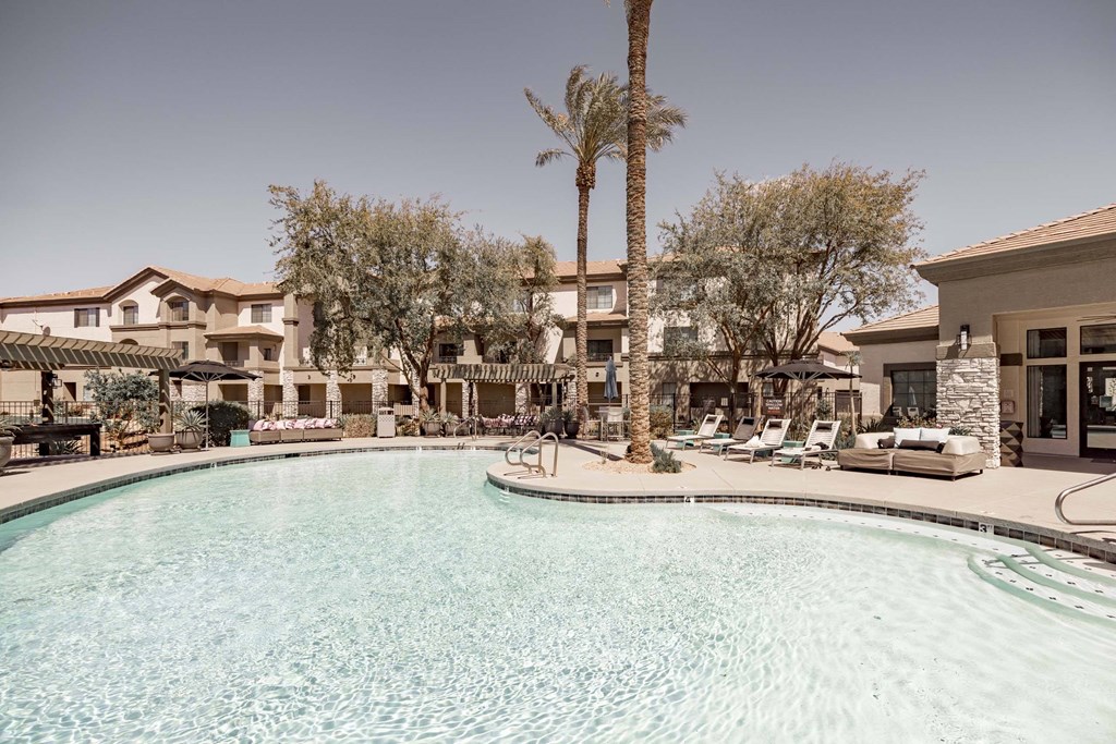 A pool surrounded by palm trees and lounge chairs.