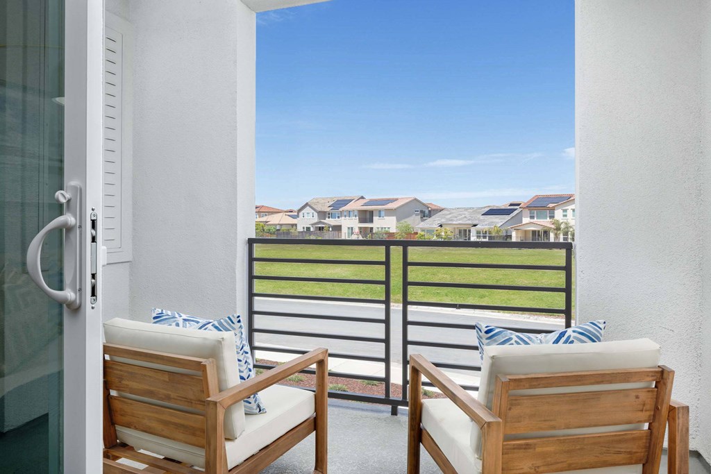 Two chairs are on a balcony with a view of a residential area.