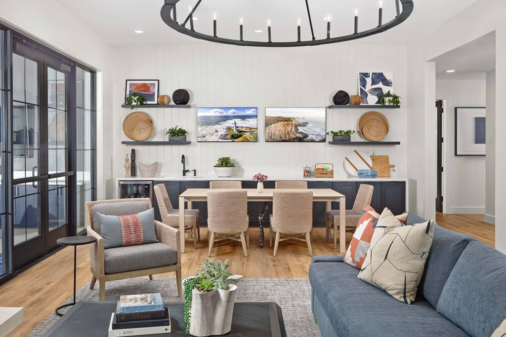 A living room with a grey couch, a grey armchair, a wooden dining table with chairs, a grey rug, a grey coffee table, a grey cushion, a grey throw pillow, a grey throw blanket