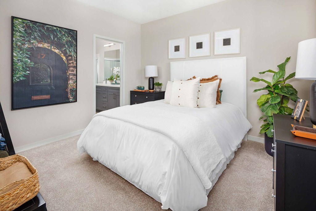 A bedroom with a white bed and a framed picture on the wall.