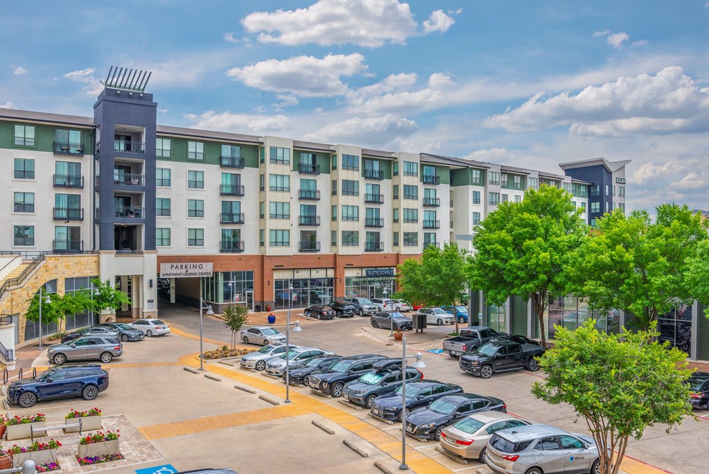 A parking lot in front of a multi-story building with cars parked.