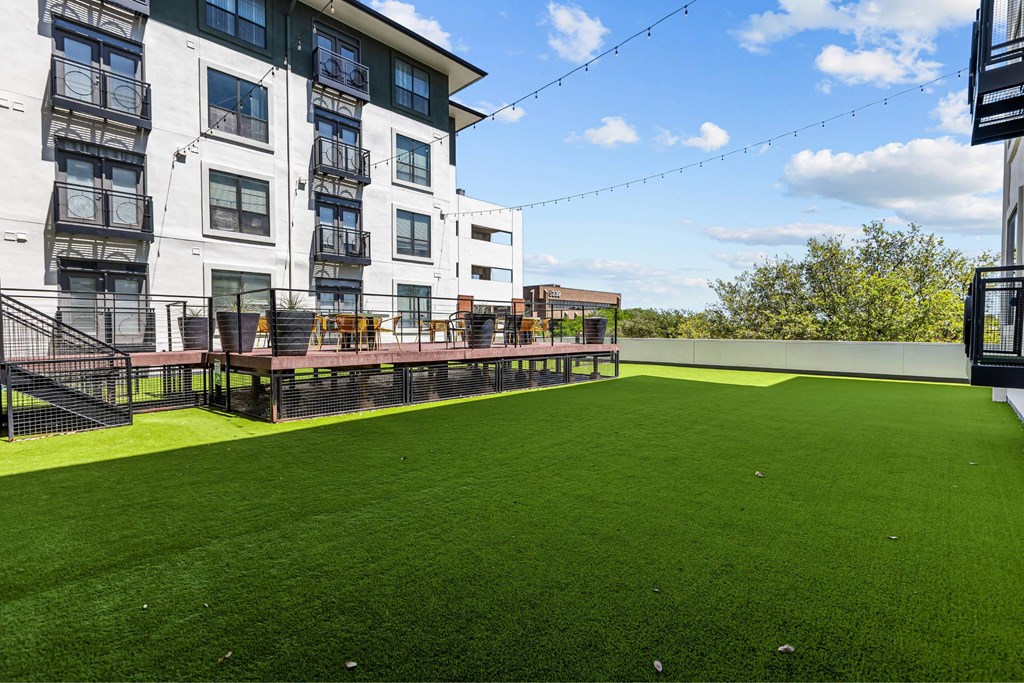A large grassy area in front of a building with a black railing and a bench.