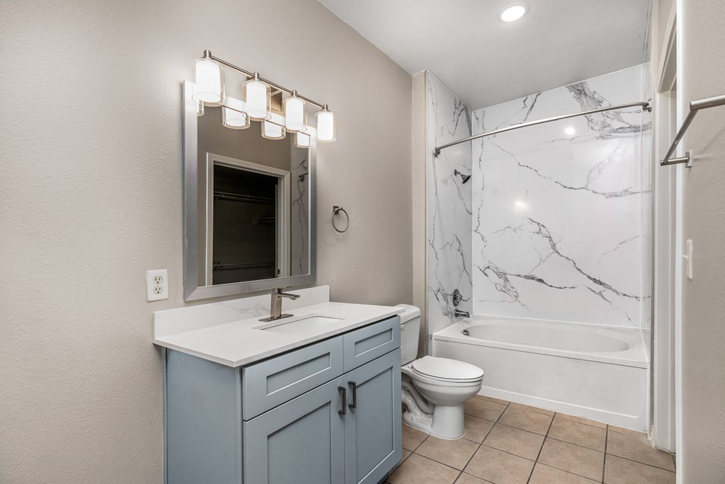 A bathroom with a marble shower and a vanity with a mirror above it.