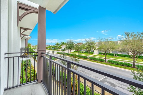 A balcony with a metal railing overlooks a street with trees and houses.