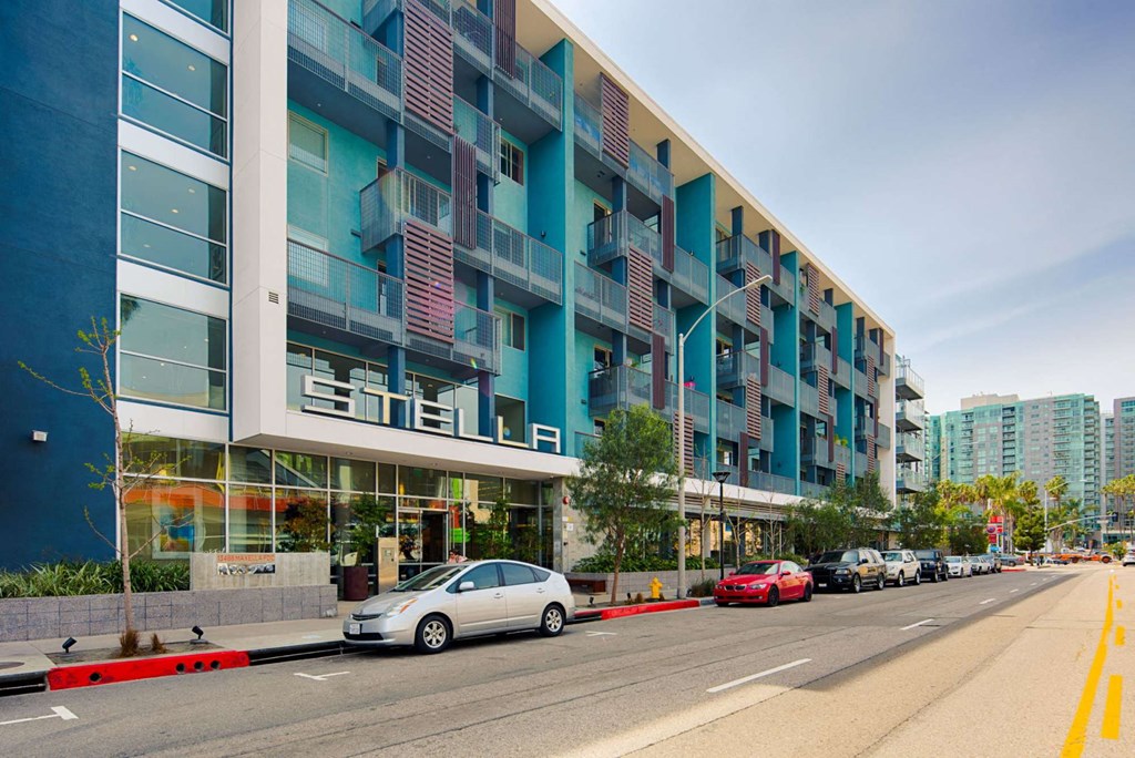 A street view of a modern building with cars parked on the side of the road.