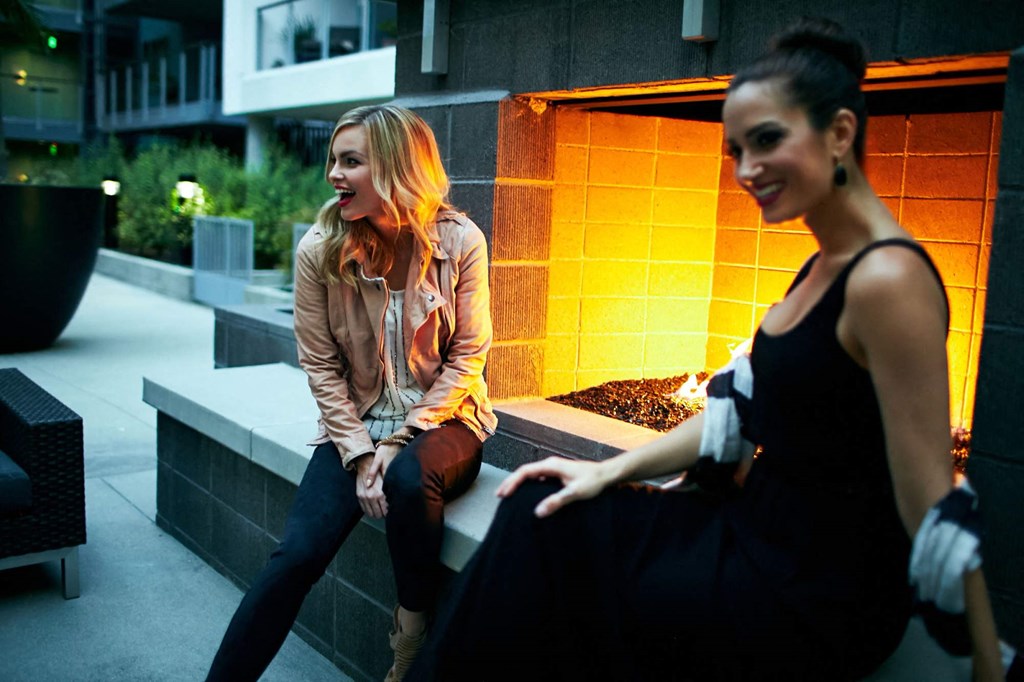 Two women sitting on a bench in front of a lit wall.