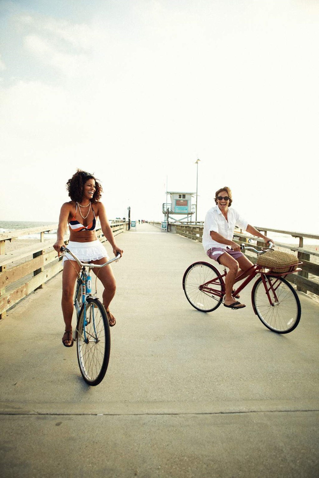 Two women riding bikes on a boardwalk.