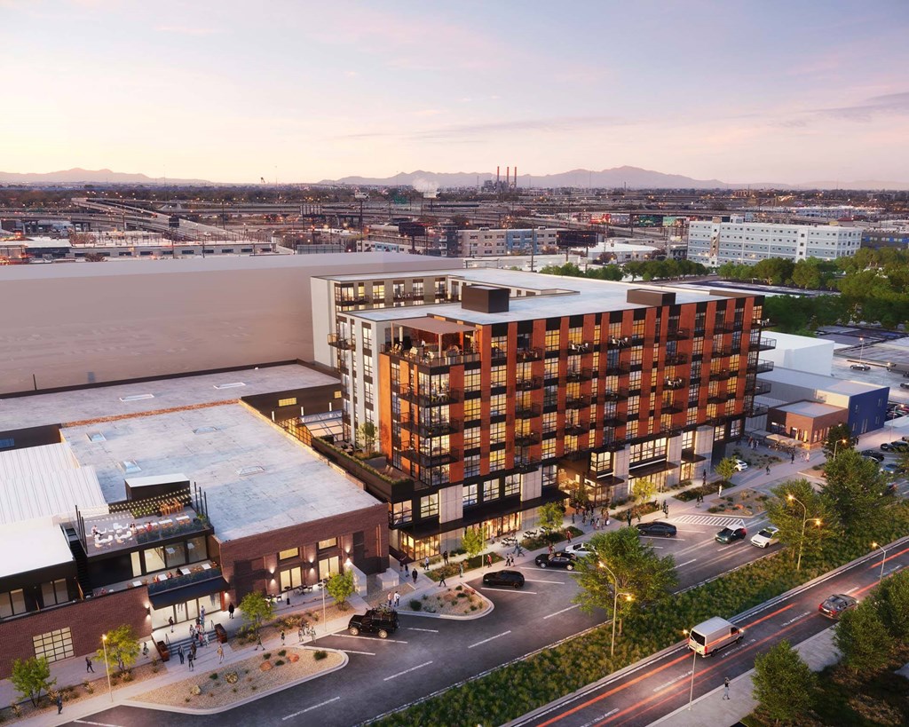 A modern building with a lot of windows is surrounded by a parking lot and other buildings.