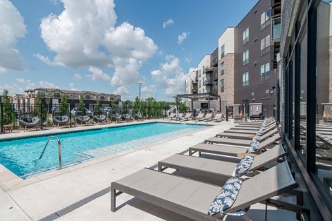 A pool with sun loungers and a building in the background.
