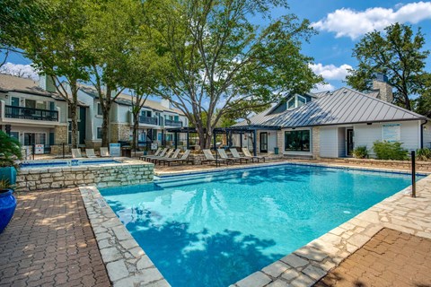 A swimming pool surrounded by a stone patio and lounge chairs.