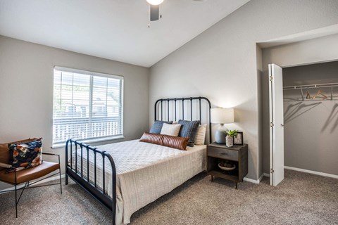 A bedroom with a bed, chair, and a window.