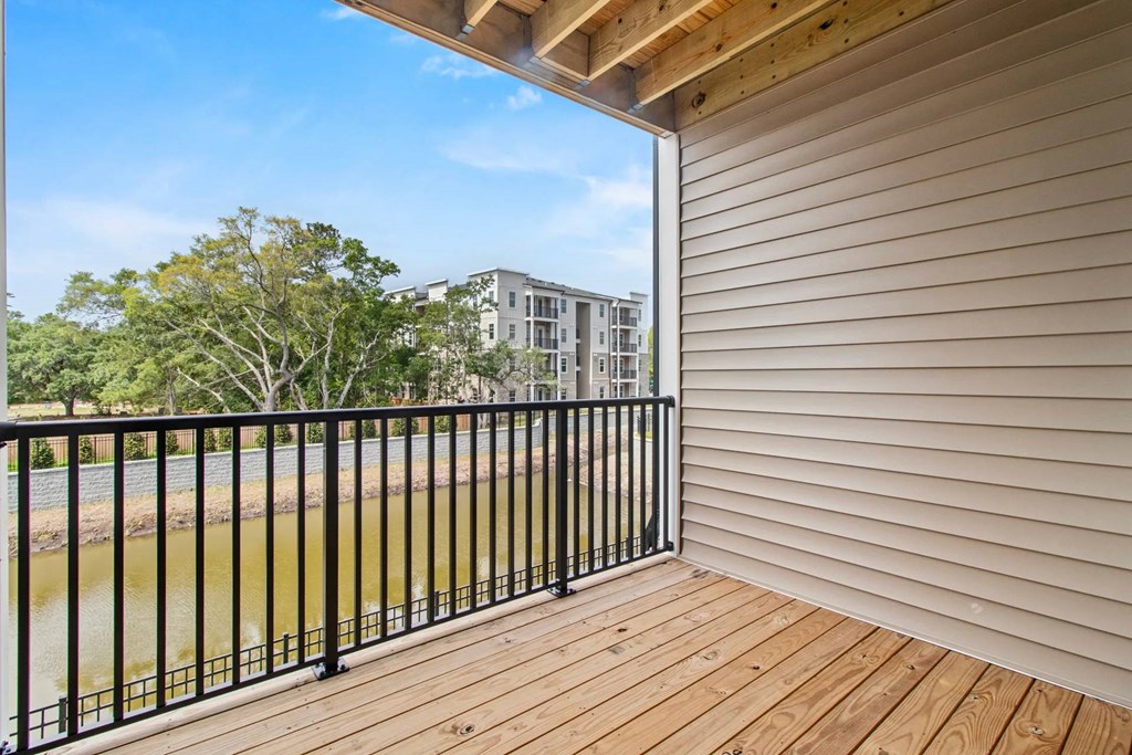A balcony with a black railing and wooden floor overlooks a body of water and buildings.