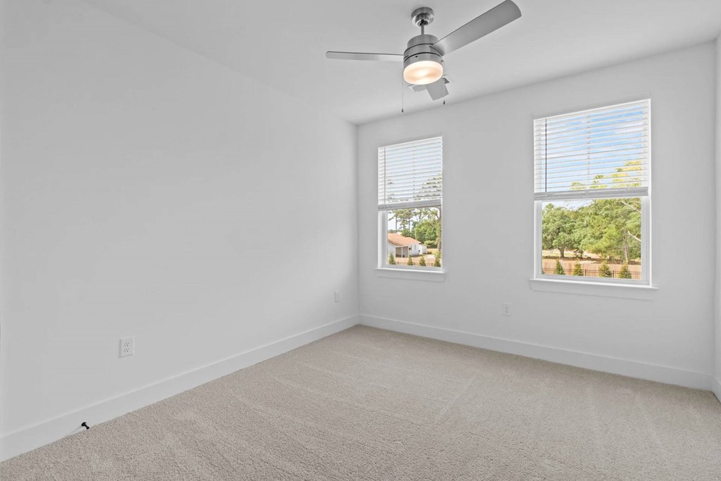 A room with a ceiling fan and two windows.