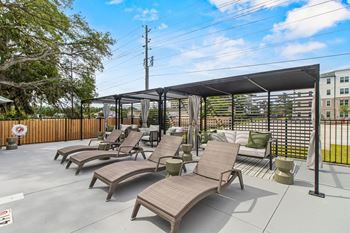 A patio with a black awning and brown chairs.