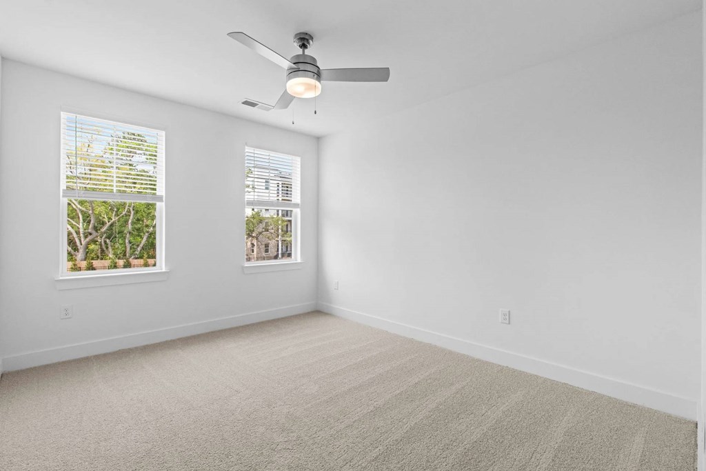 A room with a ceiling fan and two windows.
