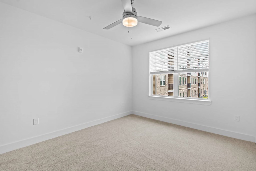 A room with a ceiling fan and a window showing a view of buildings outside.
