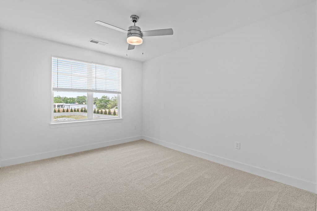 A room with a ceiling fan and a window showing trees outside.