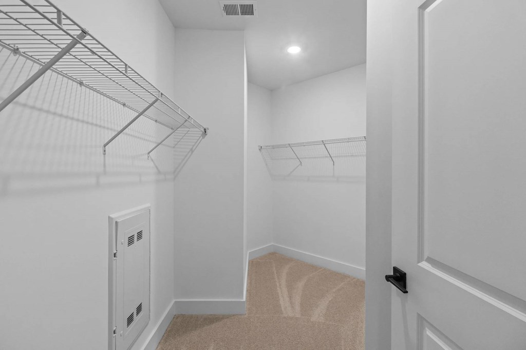 A white walk in closet with a carpeted stairway.