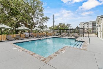 A large outdoor swimming pool surrounded by a fence and lounge chairs.