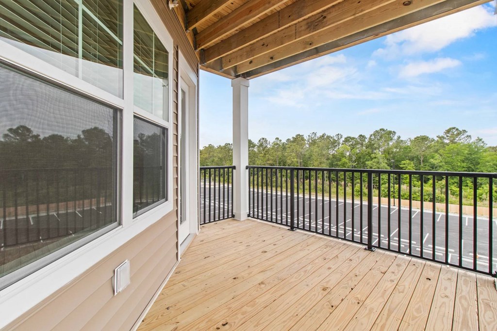 A wooden deck with a black railing and a view of a road and trees.